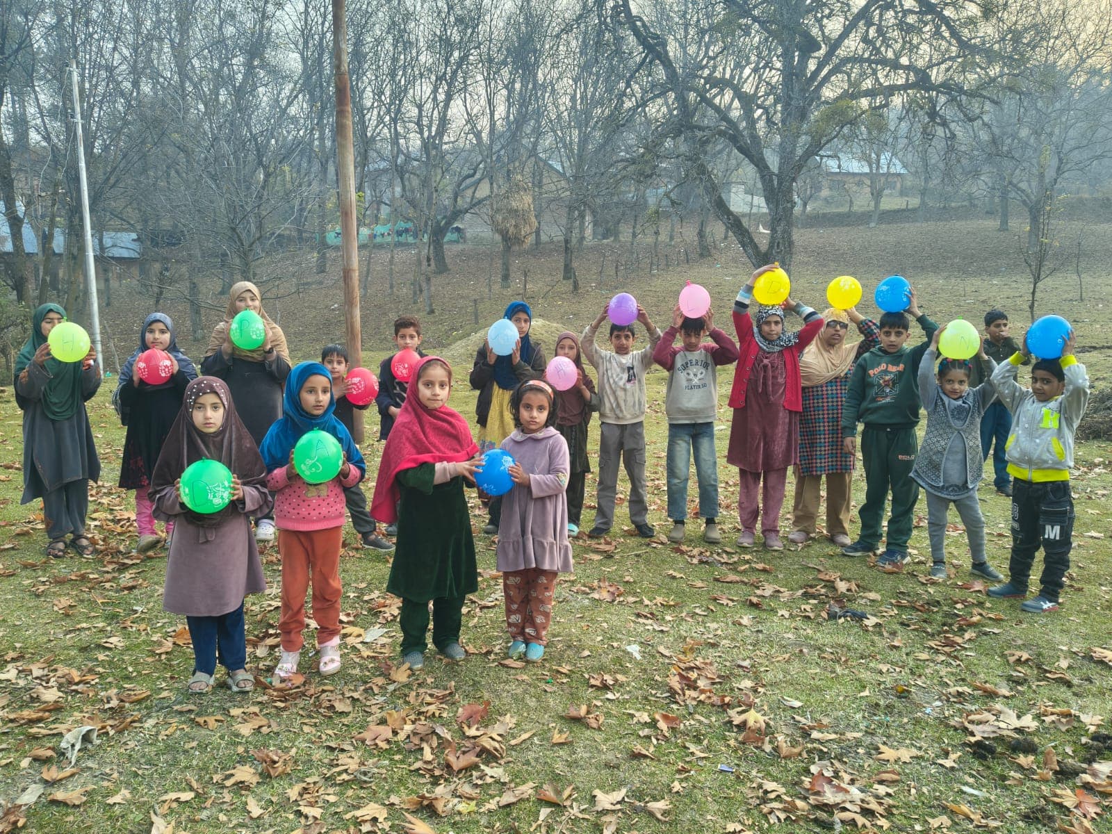 Children holding lettered balloons above their heads in an orchard