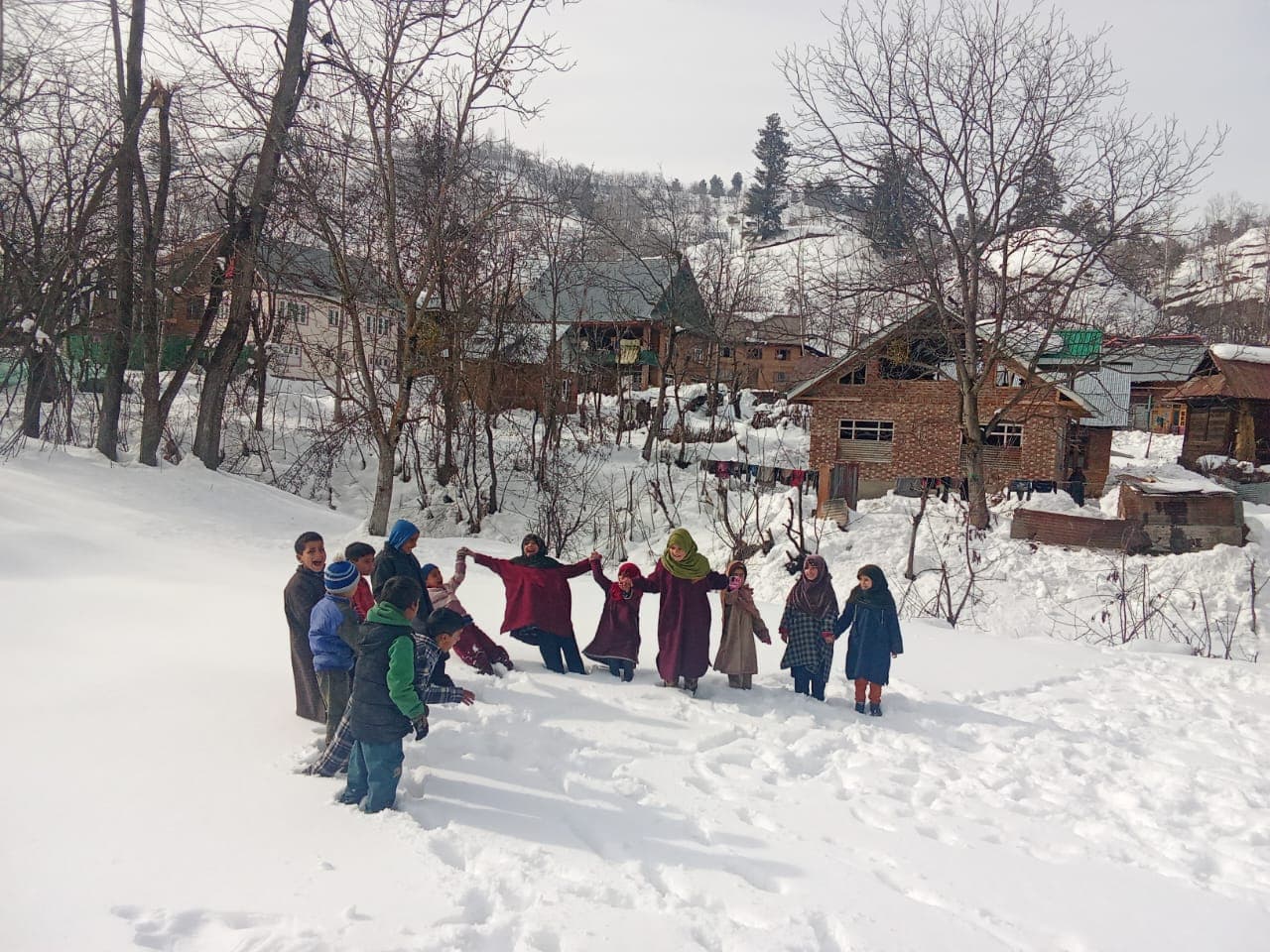 Children holding hands in deep snow in front of village houses during winter